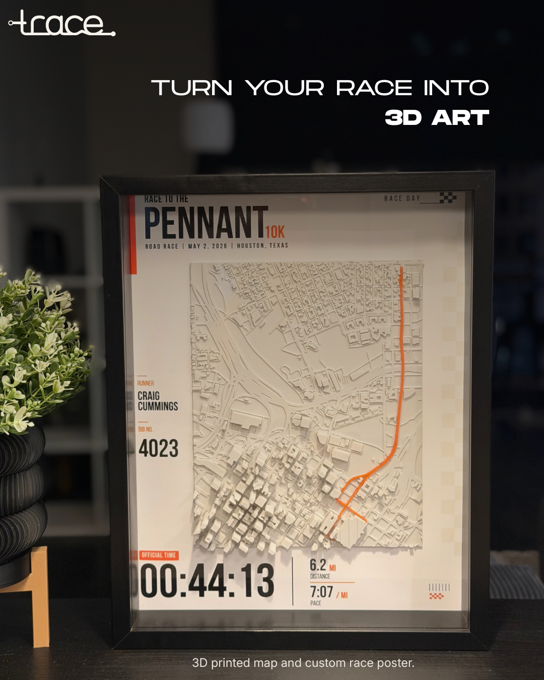 Framed Gallery Pennant 10K Trace with raised city map and orange route displayed beside a plant.