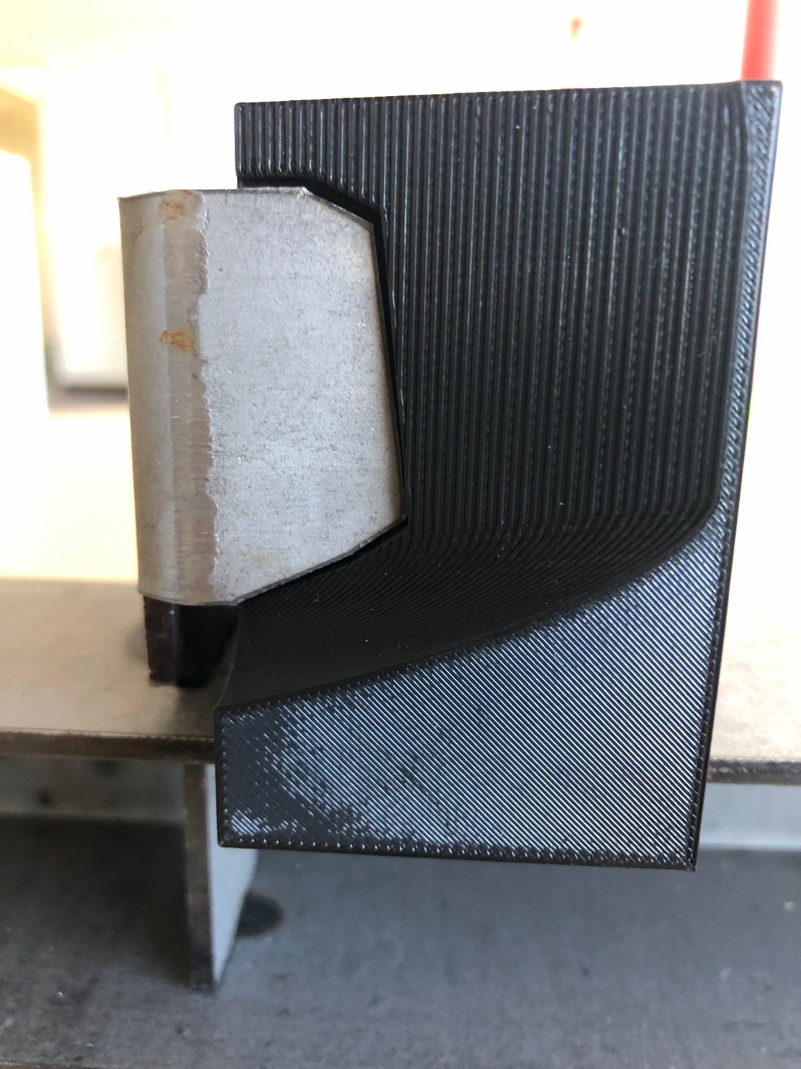 Black 3D-printed trench drain prototype fitted against a metal component during a fitment check.